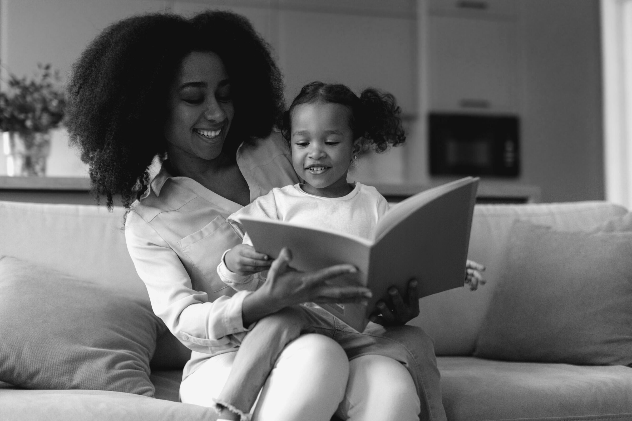 A parent and young child read a book together on a sofa at home