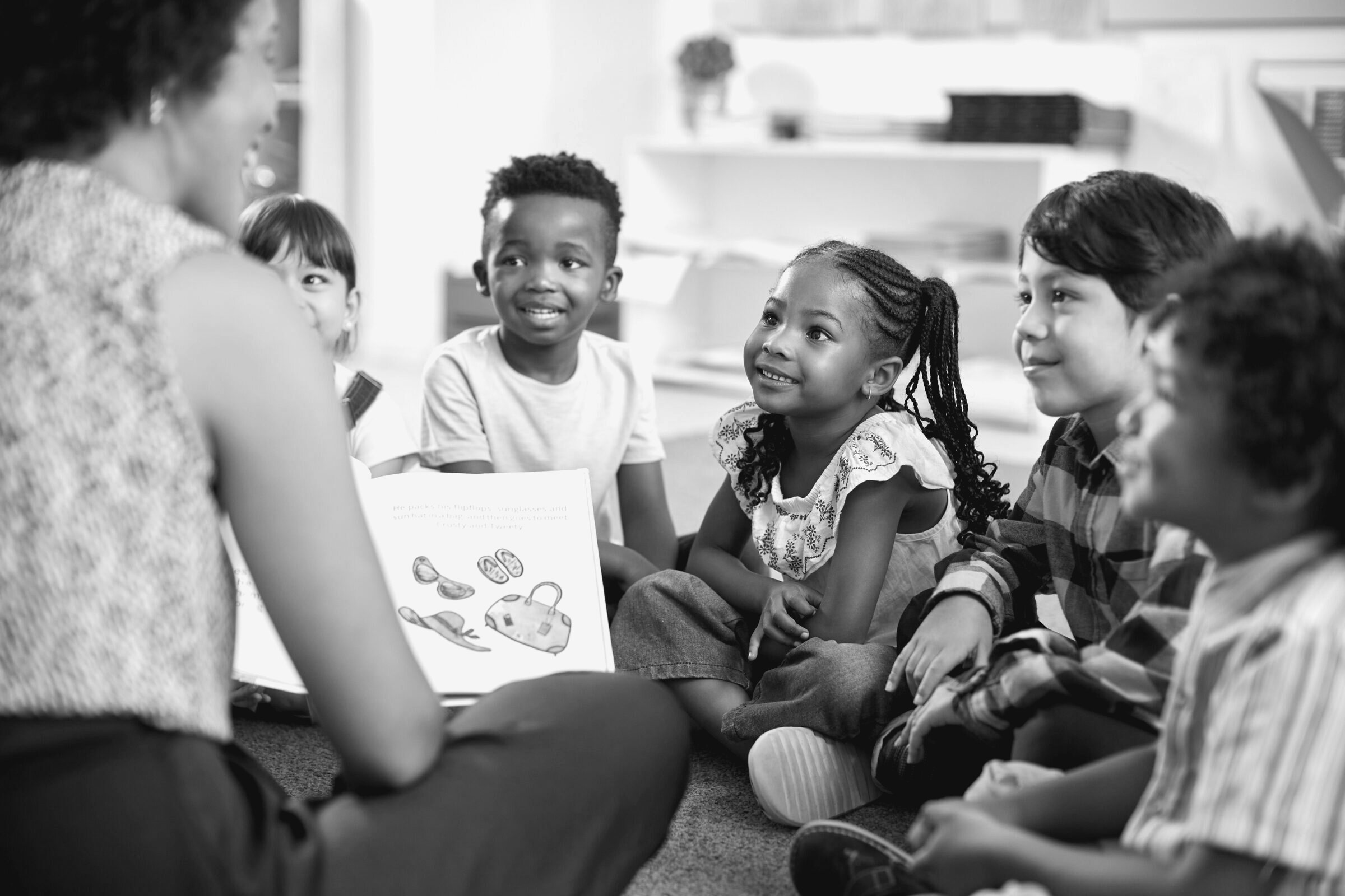 An educator reads a picture book aloud to a group of young children seated on the floor