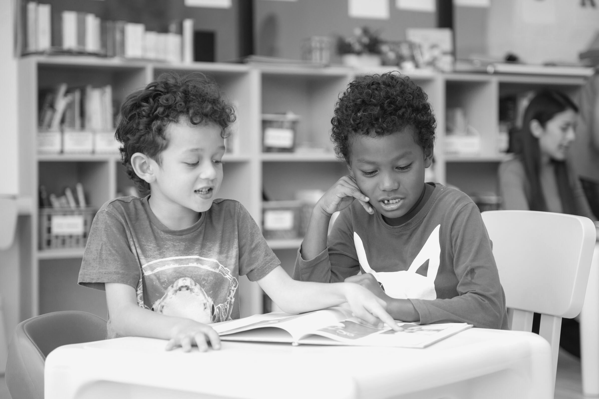 Two children share a picture book at a table in a library