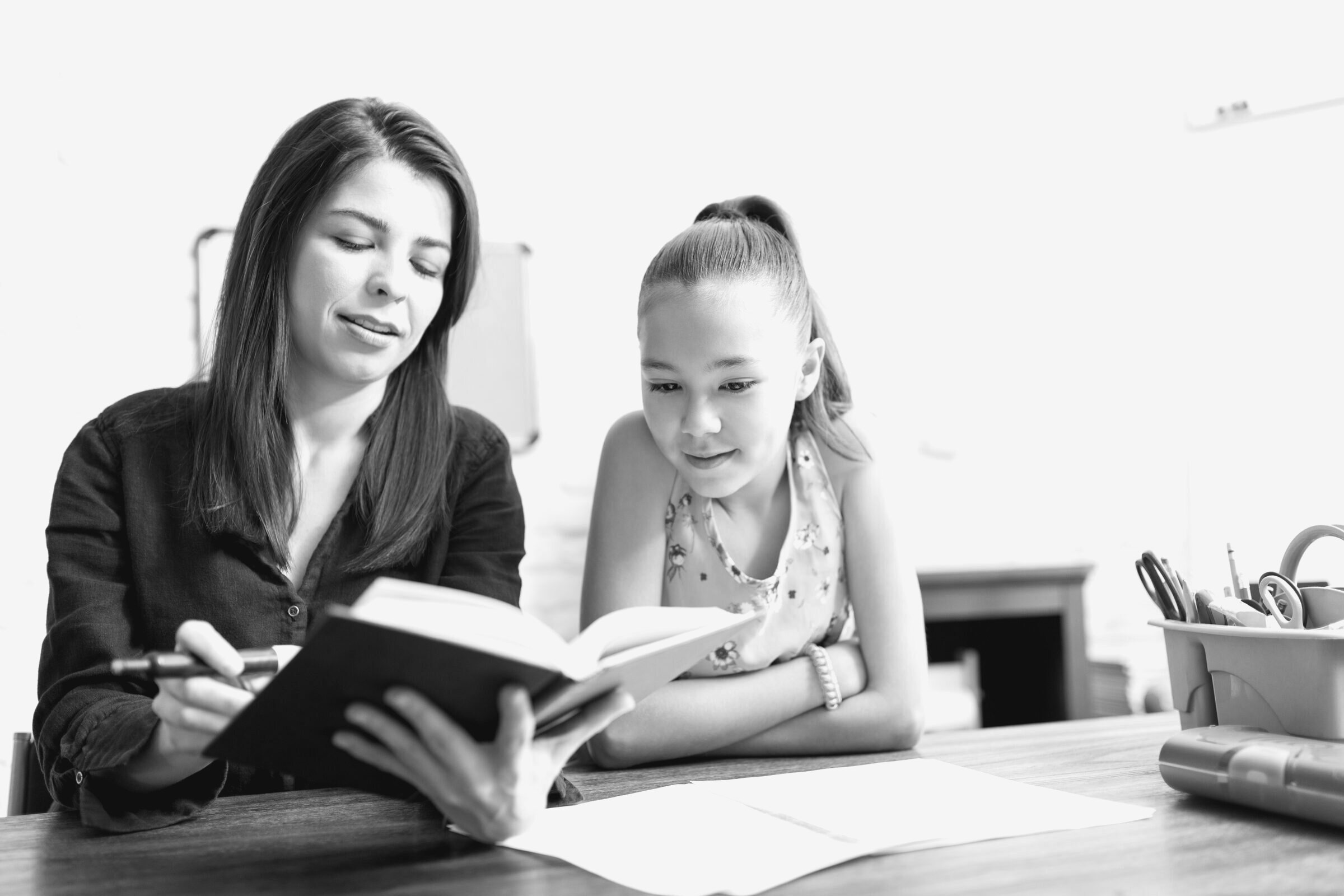 An adult and a child read a book together at a table